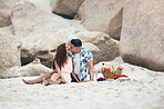 Couple, beach and love on picnic, kiss and happy together on sand by rock. Man, woman and smile with happiness on face with lips, basket and flowers to relax, vacation and travel in summer in Sydney