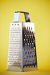 Metal or steel cheese grater for grocery cooking, food preparation and culinary help or support. Silver, metallic or home kitchenware appliance with cut pattern shredder isolated on yellow background