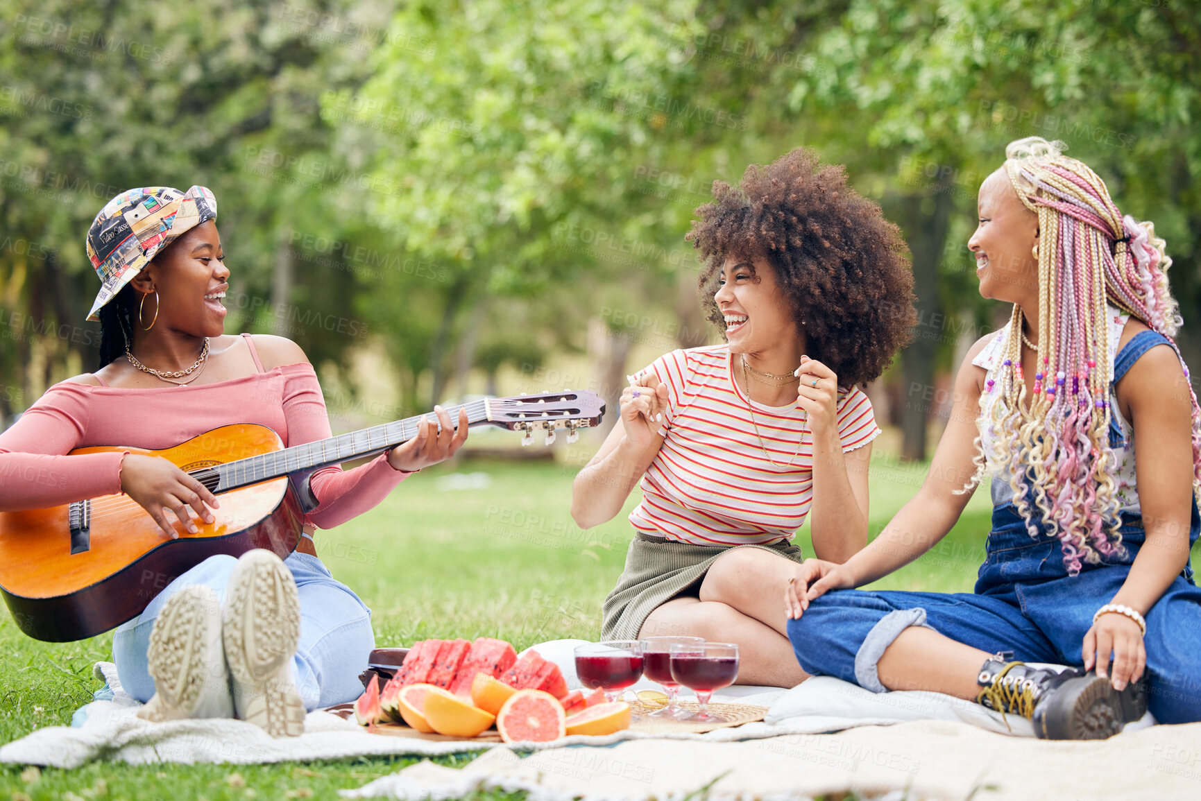 Buy stock photo Music, comic and friends on picnic in a park with food and singing with a guitar together in summer. Funny, playful and African women with smile for musician, instrument and lunch on grass in nature