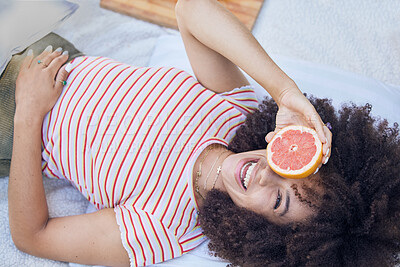 Buy stock photo Fruit, picnic and summer with a happy black woman holding a grapefruit while lying on a blanket outdoor. Food, health and wellness with a female laughing or joking while outside to relax from above