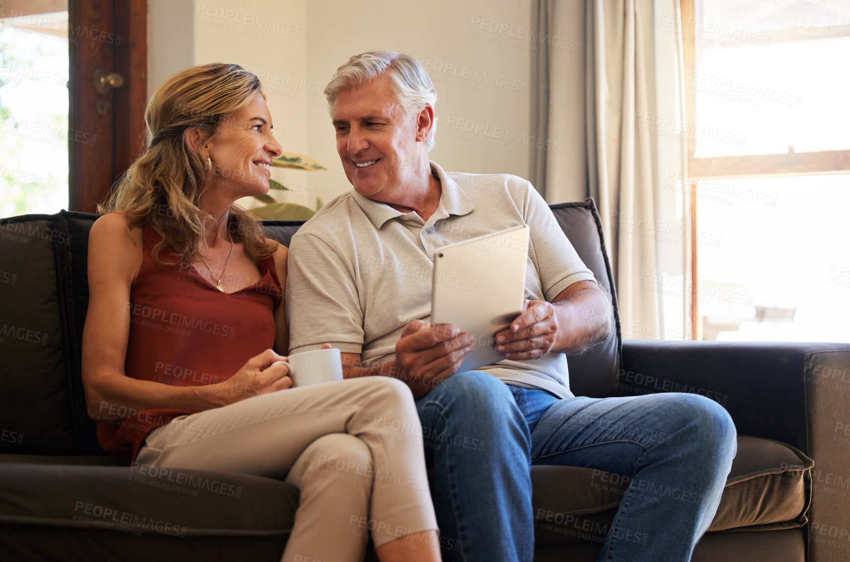 Buy stock photo Tablet, social media and senior couple with smile for choice of movie on the web with coffee on sofa of their house. Elderly man and woman talking about show on subscription service on tech with tea