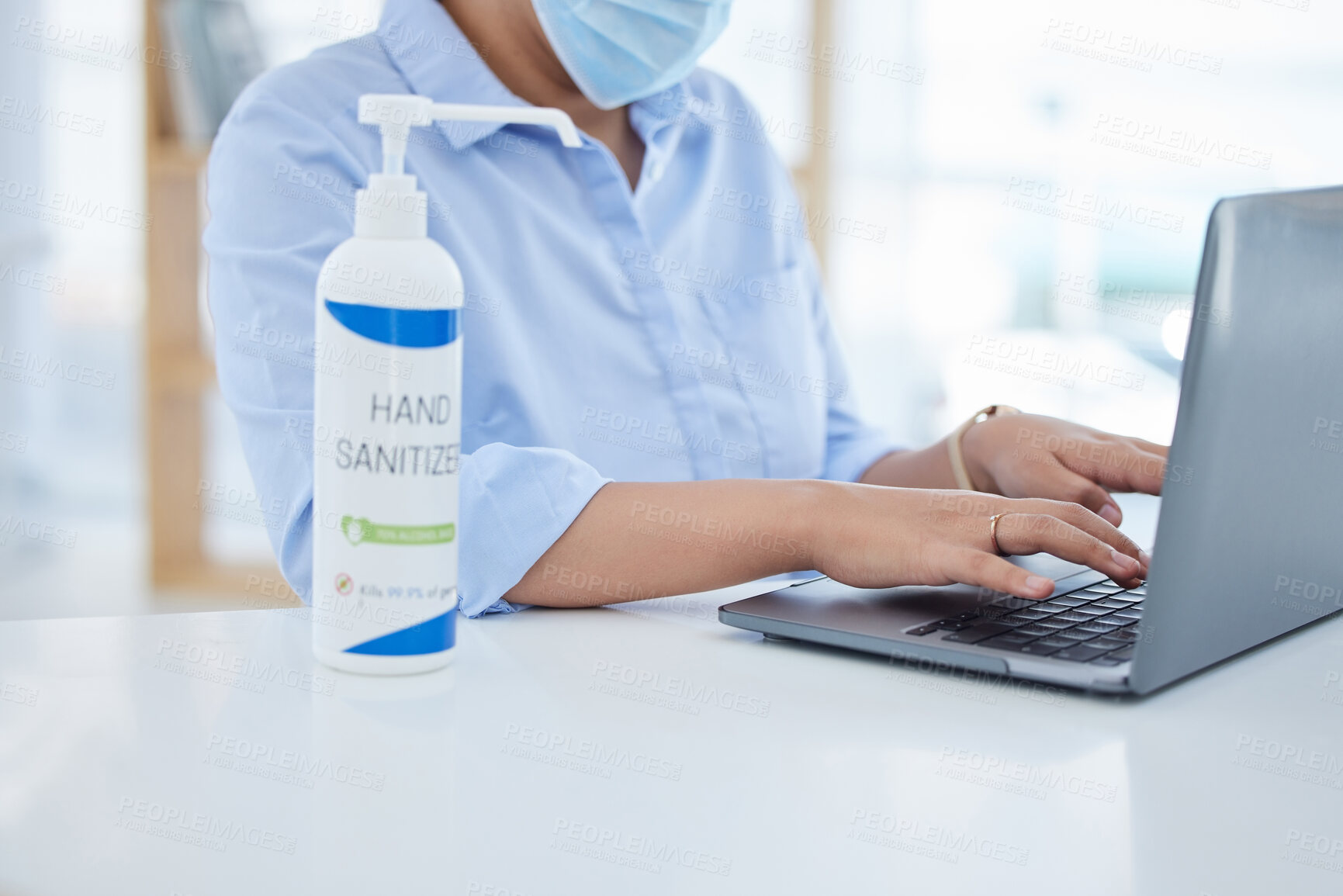 Buy stock photo Covid, hand sanitizer and a woman in office typing on laptop with face mask. Online work, hygiene and businesswoman with alcohol spray on desk. Virus prevention, safety and cleaning hands in pandemic