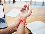Man, touch wrist and with pain at desk busy working, from planning or writing in workplace. Painful, male, holding hand or injury overworked from typing on laptop at work table in office or workspace