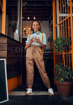 Buy stock photo Cafe, student and phone social media with headphones on walk commute break in New York city. Happy urban college girl enjoying internet leisure on smartphone at doorway of local business.

