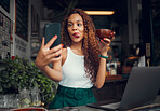 Selfie, coffee shop and funny with a woman customer using a laptop and phone in her local cafe. Silly, face and mobile with a young female positing a photograph to the internet while in a restaurant