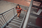 Woman with headphones walking on stairs in city listening to music and smile on face. Fashion, beauty and young girl in urban town with earphones for streaming song, track and radio and taking a walk