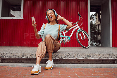 Buy stock photo Happy woman, phone and headphones for music or listening to podcast while sitting on a urban city street singing a song with a bike to travel. Female using technology to stream audio on a sidewalk