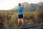 Phone, nature and fitness with a man taking a photograph while out for a sports run in the wilderness with a view. Exercise, training and workout with a picture of the mountains taken by male athlete