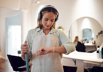 Buy stock photo Watch, headphones and woman cleaning salon while streaming music, podcast or radio. Break, cleaner and female from Canada sweeping workplace, looking at time and listening to audio, song or album.

