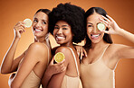 Diversity, beauty and friends, women and lemon for skincare, wellness and health on orange studio background. Smile, models and fruit, lemons or lime citrus for vitamin c, nutrition and healthy skin.