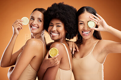 Buy stock photo Diversity, beauty and friends, women and lemon for skincare, wellness and health on orange studio background. Smile, models and fruit, lemons or lime citrus for vitamin c, nutrition and healthy skin.
