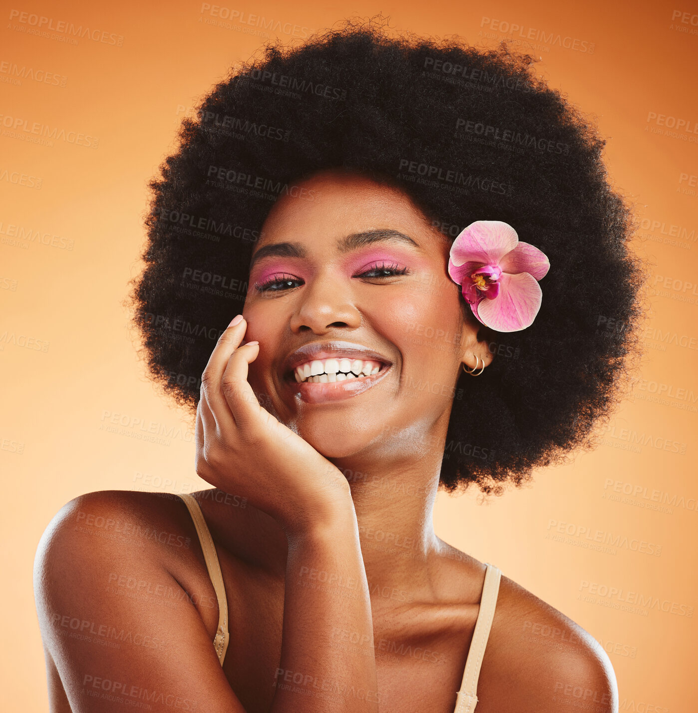 Buy stock photo Face, beauty and black woman with flower in afro hair on orange studio background. Portrait, skincare and happy woman or female model from Nigeria in pink makeup, cosmetics and orchid in healthy hair