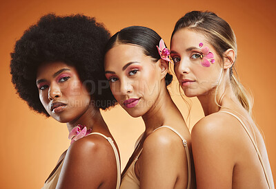 Buy stock photo Skincare, flowers and beauty portrait of women in studio for feminism, woman empowerment and cosmetics. Diversity, face and group of beautiful natural models with floral standing by orange background