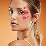 Model, eye and flower for makeup at studio for portrait, art and natural beauty. Girl, eyes and flowers with floral organic cosmetics on skin with shine, glow and healthy face with orange backdrop