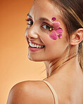 Beauty, makeup and creative with woman petals on face for design, flowers and natural cosmetics against orange background in studio. Spring, skincare and smile with girl for color, model and orchid