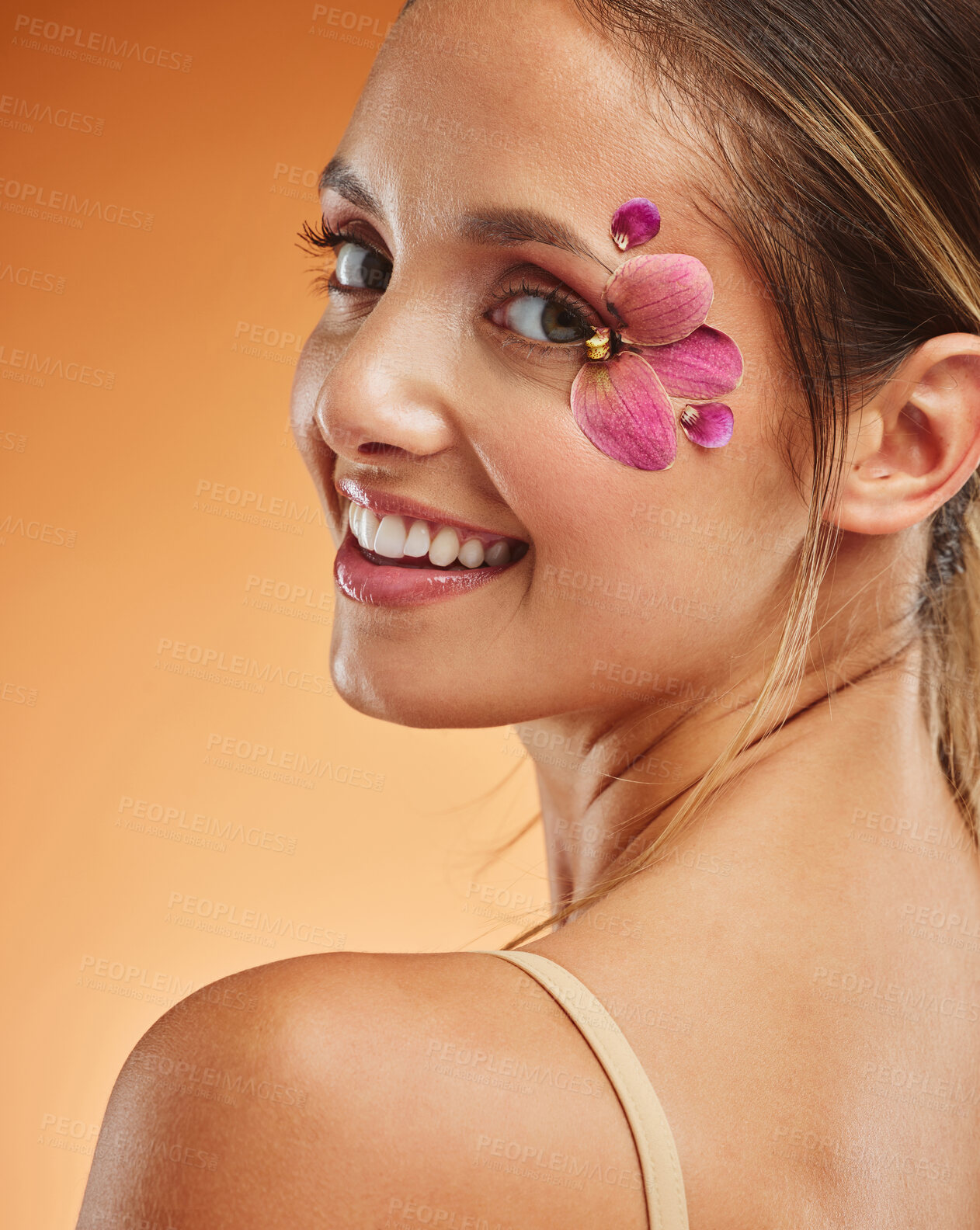 Buy stock photo Beauty, makeup and creative with woman petals on face for design, flowers and natural cosmetics against orange background in studio. Spring, skincare and smile with girl for color, model and orchid