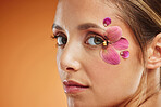 Model, flower and eye for makeup at studio for beauty, art and portrait with smile. Woman, flowers and eyes for cosmetics on skin in studio with glow, shine and healthy face with orange background