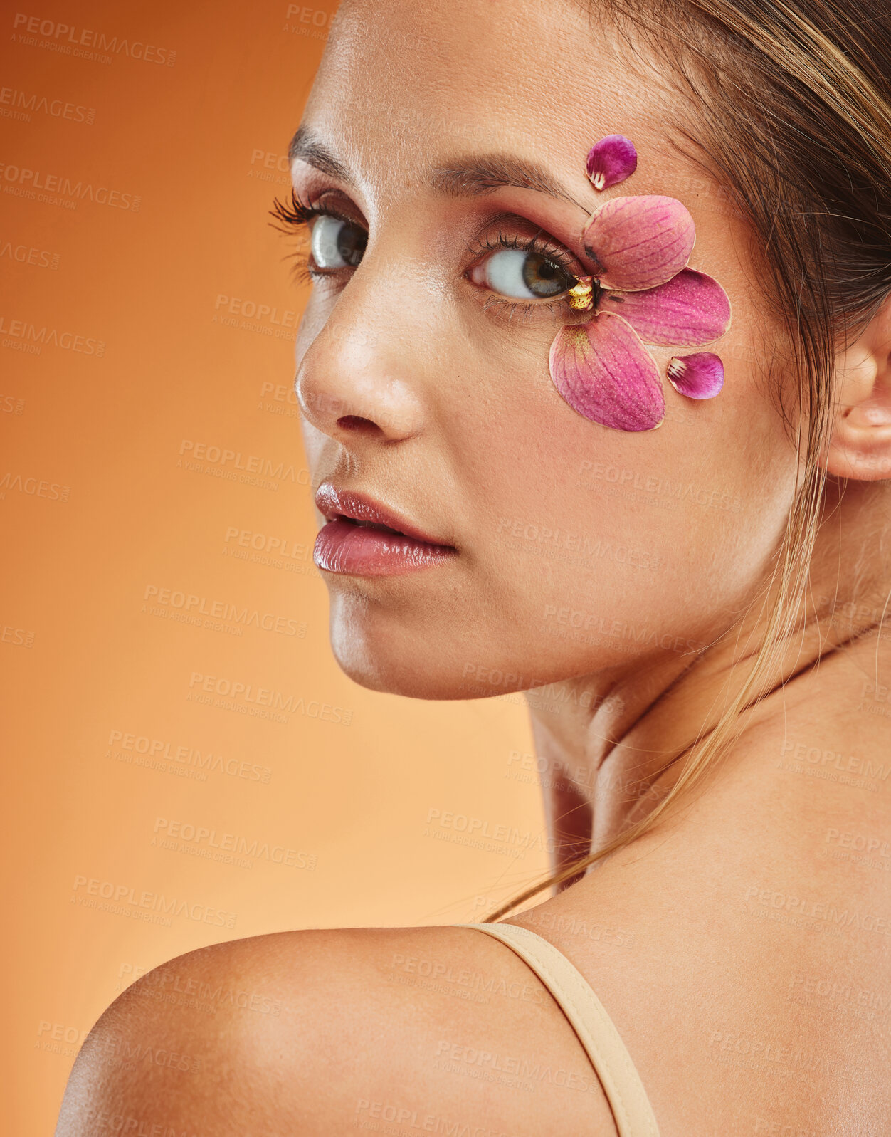 Buy stock photo Model, eye and flowers with makeup in studio portrait for fashion, cosmetics or beauty against backdrop. Woman, art and flower with petals on skin for skincare, happy and face orange background