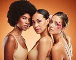 Women, flowers and beauty in makeup, diversity and models on orange studio background. Cosmetic, skincare and happy, young and elegant female friends with cosmetics posing together with orchid plant