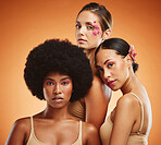 Makeup, women and beauty, diversity and flowers on orange studio background. Models, friends and females posing together with serious facial expression, orchids and floral plants on hair and face.