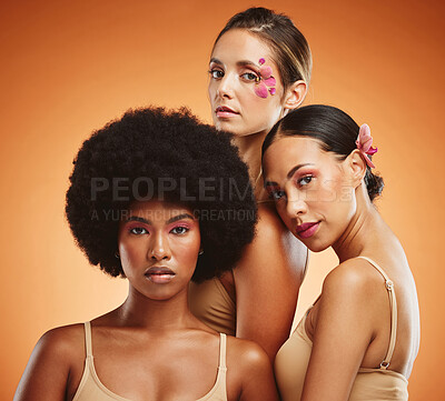 Buy stock photo Makeup, women and beauty, diversity and flowers on orange studio background. Models, skincare and friends together with serious facial expression, organic cosmetics or empowerment with floral orchids