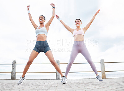 Jumping jack, fitness and women training cardio, happy with workout and smile during exercise in the city by the ocean. Young friends with energy for sports collaboration and stretching in the street