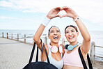 Hands, heart and fitness while woman friends gesture a hand sign outdoor during fitness or exercise by the ocean. Nature, training and love with female sports people by the sea for a workout