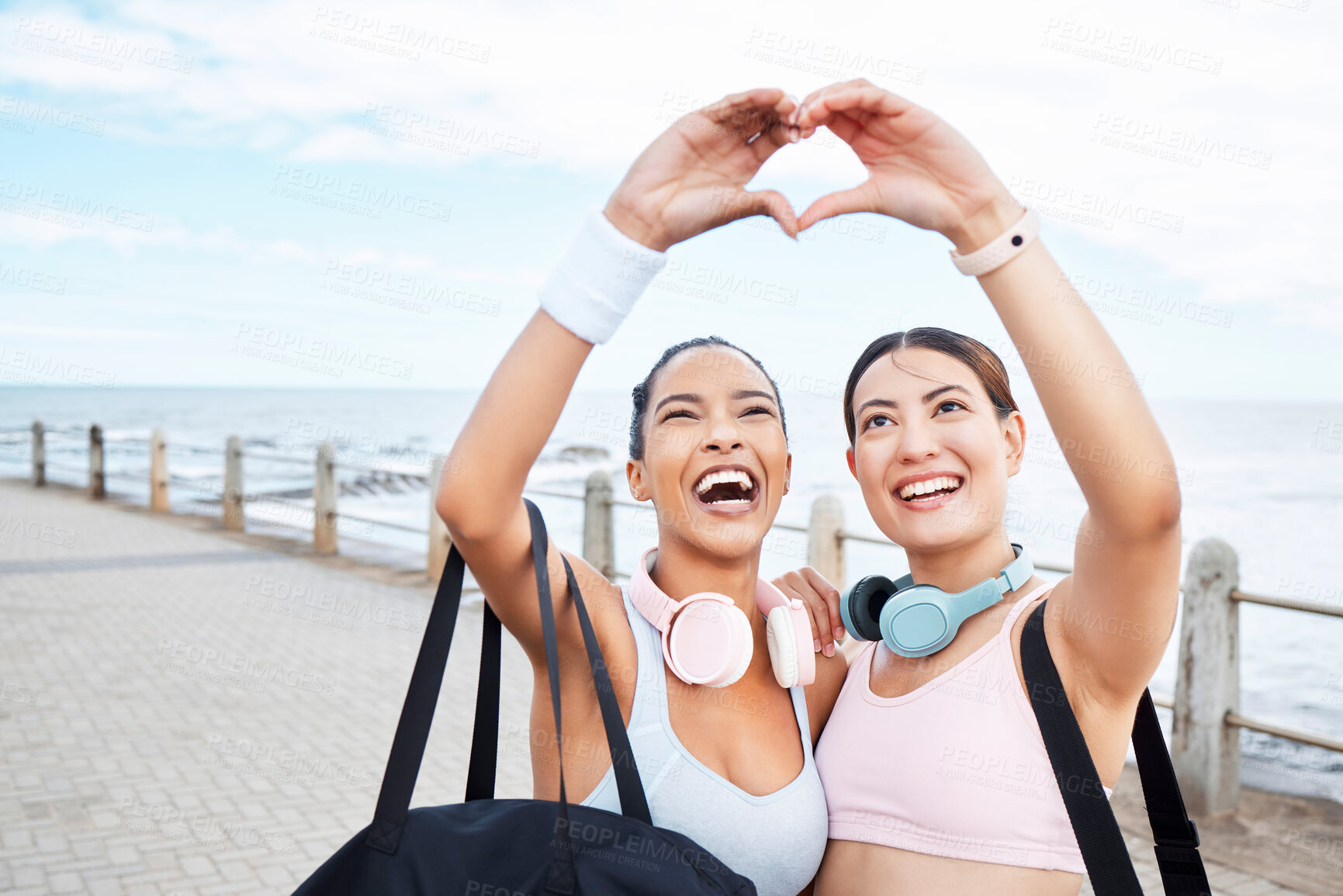 Buy stock photo Hands, heart and fitness while woman friends gesture a hand sign outdoor during fitness or exercise by the ocean. Nature, training and love with female sports people by the sea for a workout