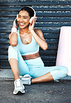 Headphones, fitness and black woman in city sitting on ground on running break. Exercise, sports and Brazilian female streaming music, radio or audio podcast on headset enjoying favorite workout song