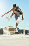 Soccer, skill and man athlete training with a ball for a game or exercise on rooftop in the city. Fitness, sports and male football player jumping to practice a trick outdoor for match in urban town.