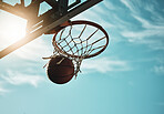 Below, basketball and net with sky in summer for shooting, scoring and points to win game. Hoop, rim and ball in closeup at basketball court for sports, competition or workout at playground, outdoor