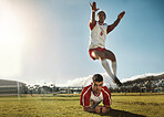 Soccer, fitness and training with a sports man jumping over his teammate during practice on a grass pitch or field. Football, workout and exercise with a male athlete exercising with his team outdoor
