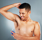 Happy, smile and man with deodorant spray for hygiene, fresh scent and fragrance after a shower. Happiness, clean and guy spraying his armpit to prevent odor or smell isolated by a gray background.