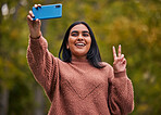 Selfie, park and young woman, peace and smartphone, pose while outdoor in nature and happy. Gen Z person from India, smile and technology, fun and youth, walking outside in garden with hand gesture.