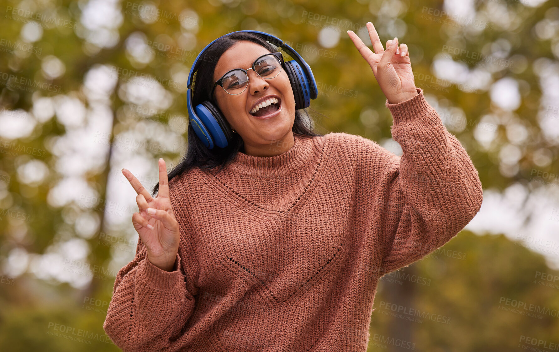 Buy stock photo Music, headphones and peace hand sign of a woman from India in nature on a walk or hike. Portrait of a person with a happy smile listening to a podcast and web streaming audio outdoor feeling free