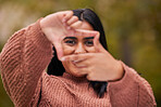 Hands frame, woman and eyes look through fingers while framing happy facial expression. Portrait of young indian girl, pose behind hand gesture and smile against blur bokeh nature background outside