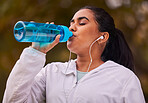 Fitness, runner and woman with bottle drinking water while running in forest for exercise, cardio workout or sports. Marathon training, thirsty or young girl with liquid hydration for wellness health