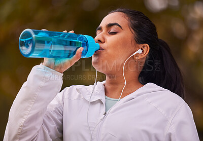 Buy stock photo Fitness, runner and woman with bottle drinking water while running in forest for exercise, cardio workout or sports. Marathon training, thirsty or young girl with liquid hydration for wellness health