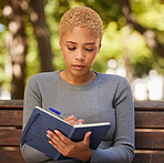 Woman, student writing in notebook and studying from diary, journal or book outdoors in park. Young girl relax alone planning schedule, write creative design idea or school vision goals on bench