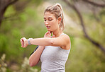 Fitness, woman and watch checking time in nature for exercise, workout or training in the outdoors. Active female runner looking at wrist monitoring heart rate, pulse or activity for healthy cardio