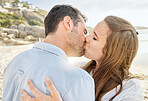 Happy, kiss and couple on a beach with love from engagement announcement or anniversary. Happiness, relax and care of a woman and man together by the sea and ocean water outdoor with commitment