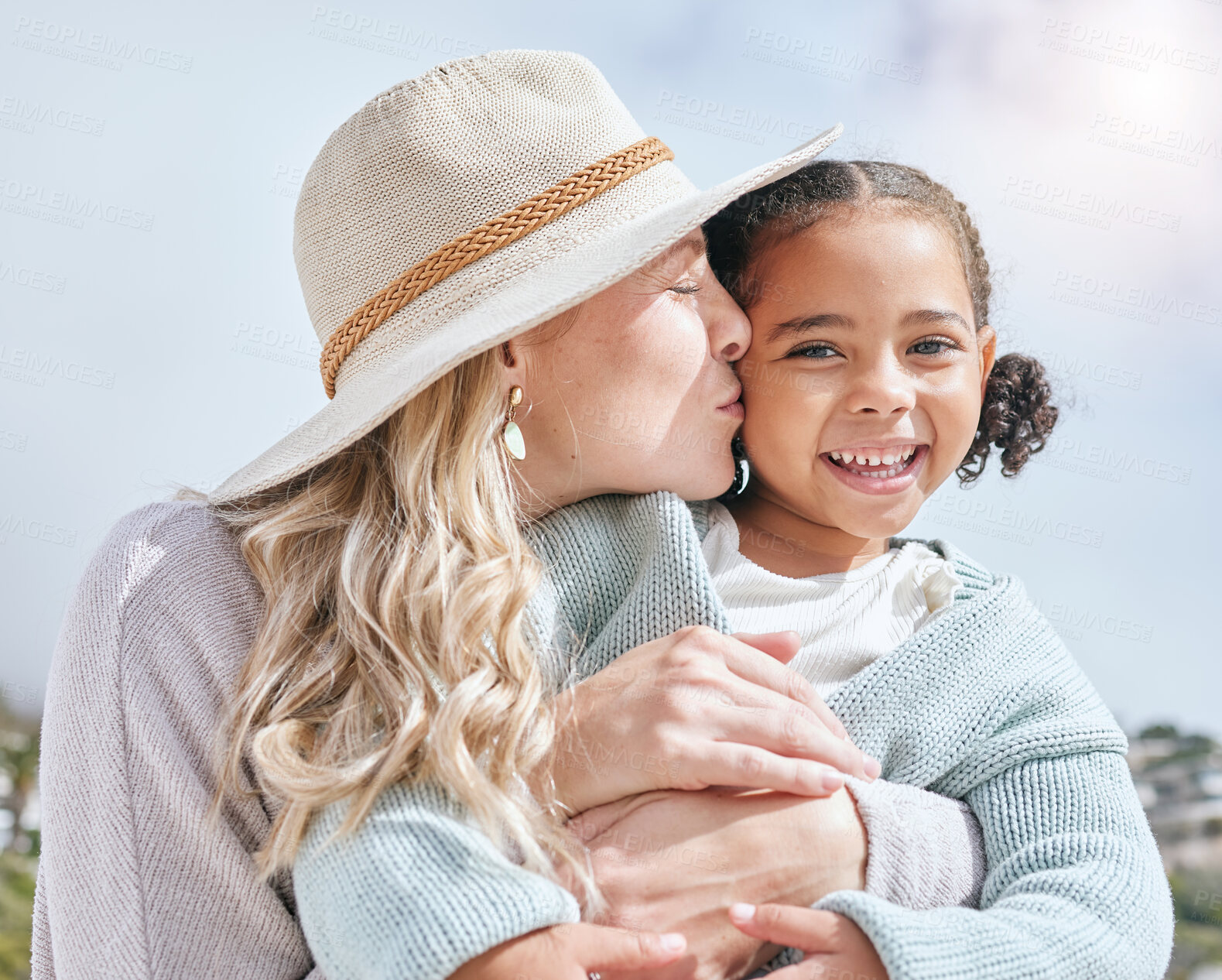 Buy stock photo Mother kiss, girl and happy face of a mama and child adoption happiness outdoor for mothers day. Portrait of a hug and love smile of a kid in the summer sun embracing the sunshine in nature 