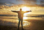 Worship, sunrise and silhouette of man at the beach standing with arms raised. Faith, religious and spiritual person looking at sun, ocean and sky in morning feeling calm, peace and hope in nature