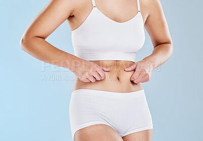 Buy stock photo Plus size, fat and woman touching her stomach cellulite in underwear standing in a studio. Overweight, obesity and closeup of a girl model feeling her chubby abdomen isolated by a blue background.