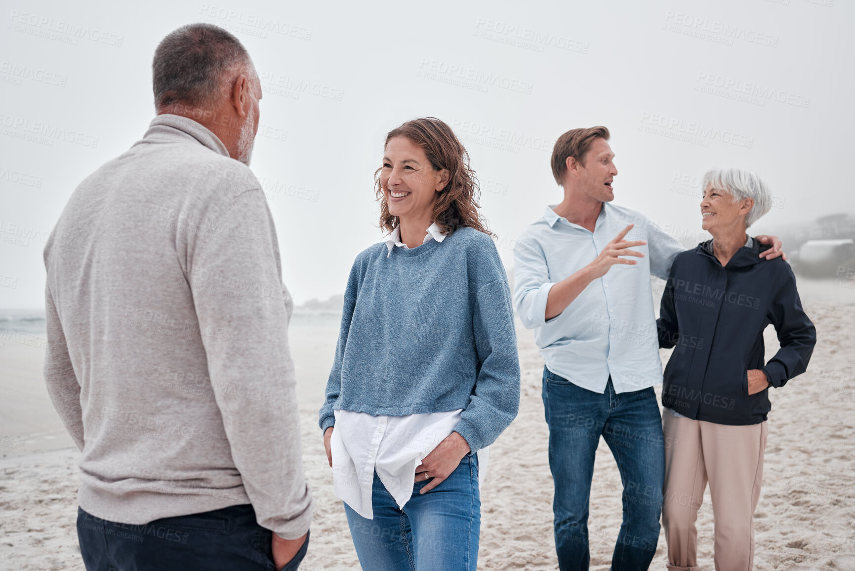 Buy stock photo Family bonding, beach and outdoor conversation of people happy spending time together. Communication of a woman, man and elderly parents on ocean sand on a cloudy day on vacation with happiness