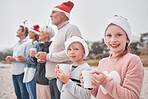 Family, generations and Christmas, drink and view outdoor while on vacation, holiday and festive time at the beach. Parents, grandparents and children, happy with hot chocolate, mug and xmas hat.