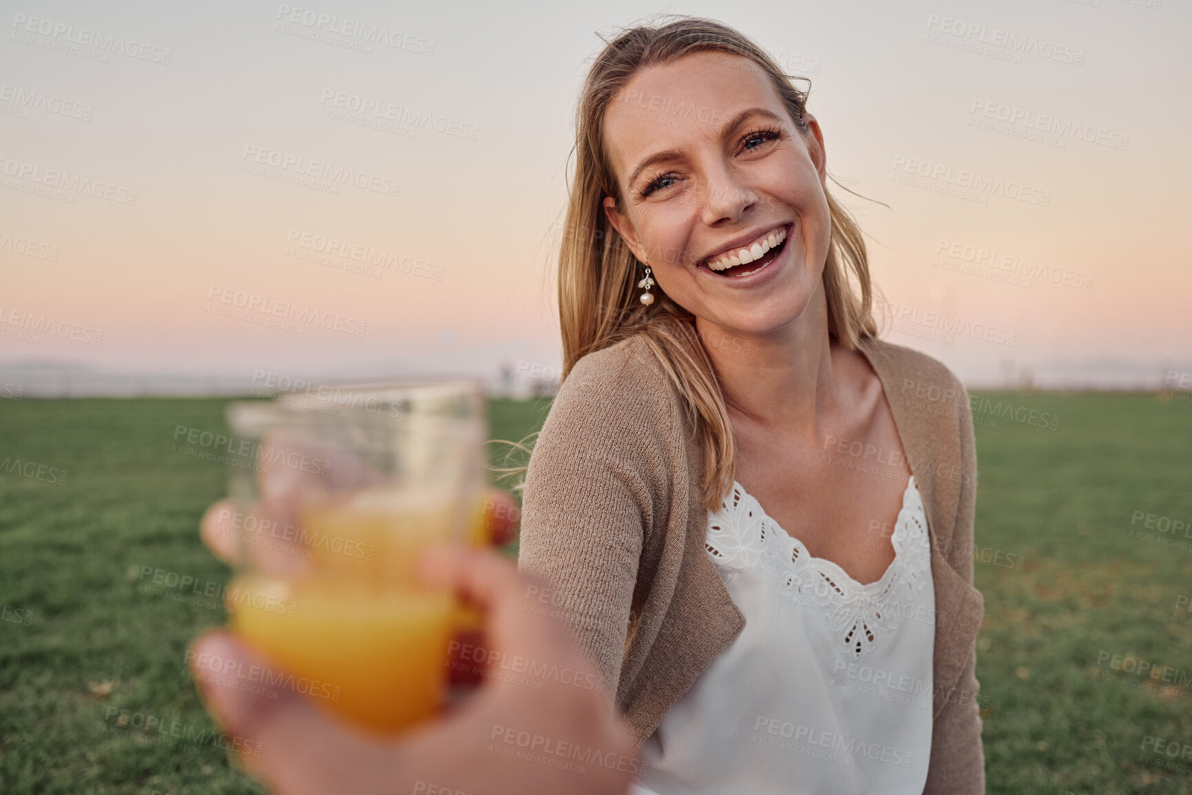 Buy stock photo Cheers, juice and portrait of a happy woman in nature on an outdoor picnic in a garden with a summer sunset. Happiness, smile and pov of a lady toasting with a orange drink while on a romantic date.