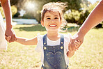 Happy, child in sun and walk in a nature park with a smile with parents holding girl hands in summer sunshine. Kid in garden, smiling on grass and family relax enjoy weekend childhood outdoor freedom