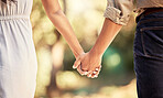 Hand, love and couple with a man and woman holding hands outdoor in care, trust and relationship. Zoom in of a male and female walking outside together for romance and affection with trust in forest