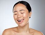 Woman face, tongue out and beauty skincare natural makeup glow. Young happy Asian girl, funny face eyes closed and healthy facial or body cosmetics for advertisement in grey studio background